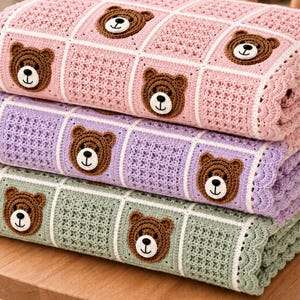 May include: A stack of three crocheted blankets in pastel pink, lavender, and sage green. Each blanket features a grid pattern with alternating textured squares and brown bear face appliques. The edges are finished with a scalloped crochet border.