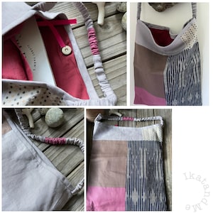 May include: A gray fabric tote bag with a pink and brown patchwork design. The bag has a drawstring closure and a long strap. The bag is made of a soft, natural fabric and has a rustic, handmade look.