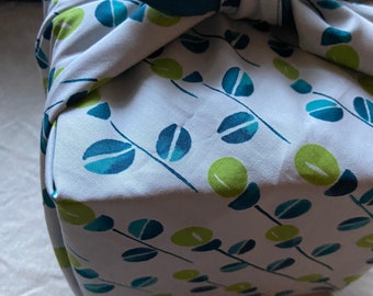May include: A white fabric gift wrap with a teal blue ribbon and a pattern of green and blue leaves.