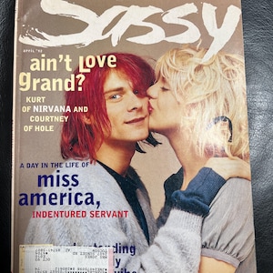 Puede incluir: El número de abril de 1992 de la revista Sassy con Kurt Cobain y Courtney Love en la portada. El texto dice: Take our sex survey, please, Sassy, ain't love grand?, Kurt of Nirvana and Courtney of Hole, y A day in the life of miss america, indentured servant.