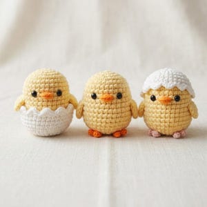 Op de afbeelding: Drie kleine, ronde, gehaakte gele kuikentjes. Het linker kuikentje zit in een witte gehaakte eierschaal. Het middelste kuikentje is geel met oranje pootjes. Het rechter kuikentje draagt een wit gehaakt eierschaaltje als mutsje op het hoofd.