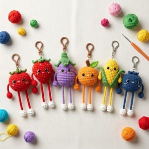 May include: Six crocheted fruit and vegetable keychains featuring a tomato, strawberry, aubergine, orange, corn, and blueberry. Each character has a round body, dangling arms and legs with white feet, and a metal lobster clasp for attachment.
