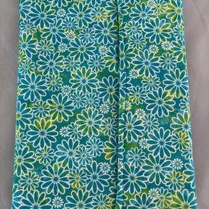May include: A folded fabric item with a teal background and a white daisy pattern with green accents. The daisies are outlined in white and densely cover the surface. The item appears to be a case or cover.