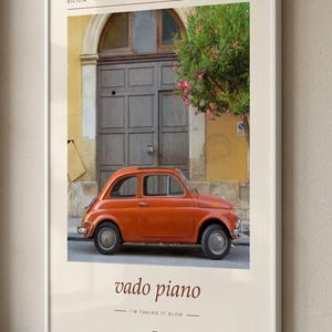 May include: A framed wall art print featuring a vintage orange car parked in front of a dark wooden door and a yellow building in Sicily, Italy. The text reads SICILIA ITALIA, vado piano, and I'M TAKING IT SLOW, with a small square icon below.