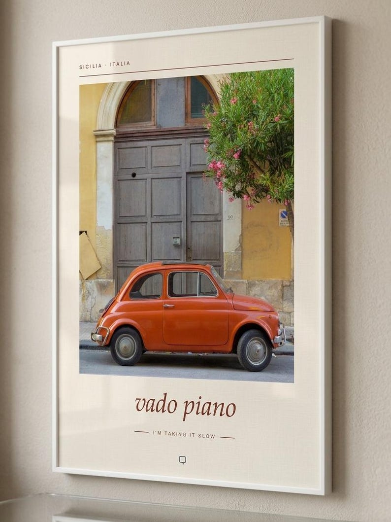 May include: A framed wall art print featuring a vintage orange car parked in front of a dark wooden door and a yellow building in Sicily, Italy. The text reads SICILIA ITALIA, vado piano, and I'M TAKING IT SLOW, with a small square icon below.