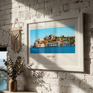 May include: A framed horizontal wall art print featuring a vibrant photograph of the Greek island Kastellorizo with colorful buildings along the water. The print includes the text Kastellorizo, Greece at the top and the phrase siga siga at the bottom.