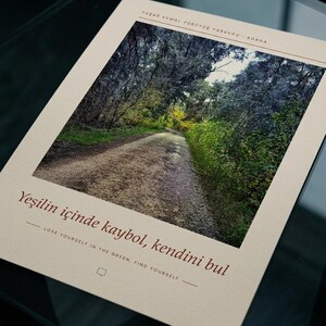 May include: A rectangular print on cream paper featuring a photograph of a gravel path winding through a dense green forest. The text reads Yaşar Kemal Y&uuml;r&uuml;y&uuml;ş Parkuru Adana, Yeşilin i&ccedil;inde kaybol, kendini bul, and Lose yourself in the green, find yourself.