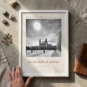 Op de afbeelding: Een ingelijste zwart-wit fotoprint van de Plaza de la Armeria in Madrid. De print bevat de tekst Plaza de la Armeria Madrid bovenaan en La luz halla el camino onderaan, met een klein tekstballon-icoontje onder de tekst.