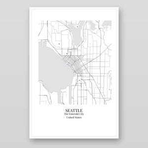 May include: A framed map print of Seattle, Washington, featuring black street lines on a white background with gray water areas and small brown dots. The text at the bottom reads SEATTLE, The Emerald City, United States.