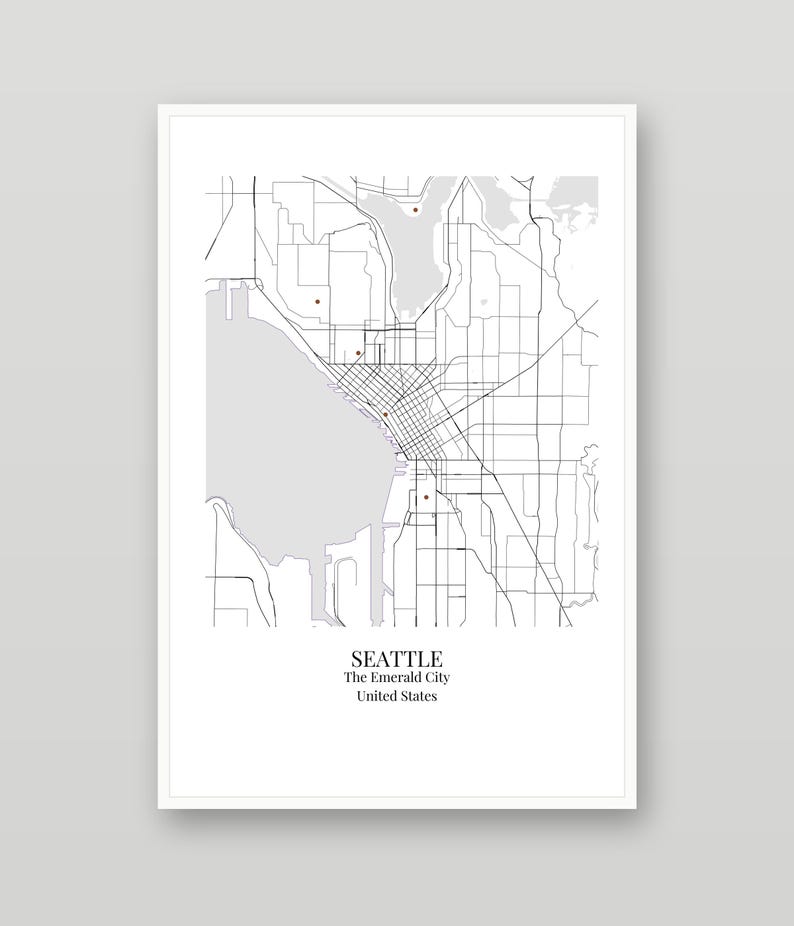 May include: A framed map print of Seattle, Washington, featuring black street lines on a white background with gray water areas and small brown dots. The text at the bottom reads SEATTLE, The Emerald City, United States.