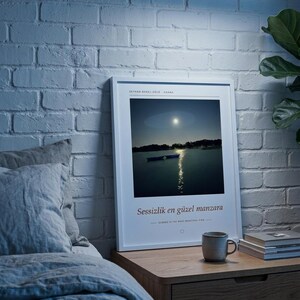 Puede incluir: Una l&aacute;mina de arte mural vertical enmarcada que muestra un paisaje nocturno de un lago con el reflejo de la luna y dos barcas. El texto dice SEYHAN BARAJ G&Ouml;L&Uuml; - ADANA, Sessizlik en g&uuml;zel manzara y SILENCE IS THE MOST BEAUTIFUL VIEW.