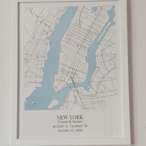 May include: A framed map print of New York City featuring light blue water, black street lines, and small red markers. Below the map, the text reads: NEW YORK, Emma & James, 40.7128&deg; N &middot; 74.0060&deg; W, October 12, 2024, in a white frame.
