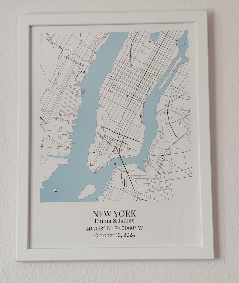 May include: A framed map print of New York City featuring light blue water, black street lines, and small red markers. Below the map, the text reads: NEW YORK, Emma & James, 40.7128&deg; N &middot; 74.0060&deg; W, October 12, 2024, in a white frame.