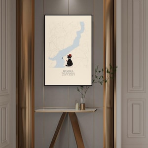 May include: A framed wall art print featuring a cream-colored map of Istanbul with a light blue Bosphorus strait. A black cat wearing a red fez sits on the shore, holding a small red tea glass. Text reads: ISTANBUL, Tea by the Bosphorus, 41.0082&deg; N, 28.9784&deg; E.
