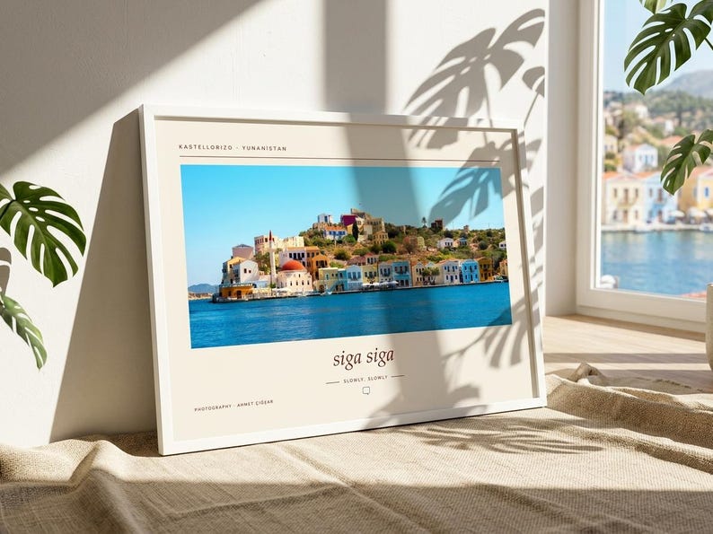 May include: A framed horizontal print featuring a vibrant photograph of the Greek island Kastellorizo with colorful buildings along the blue water. The print includes the text KASTELLORIZO - YUNANISTAN, siga siga, SLOWLY, SLOWLY, and PHOTOGRAPHY AHMET CİĞER.