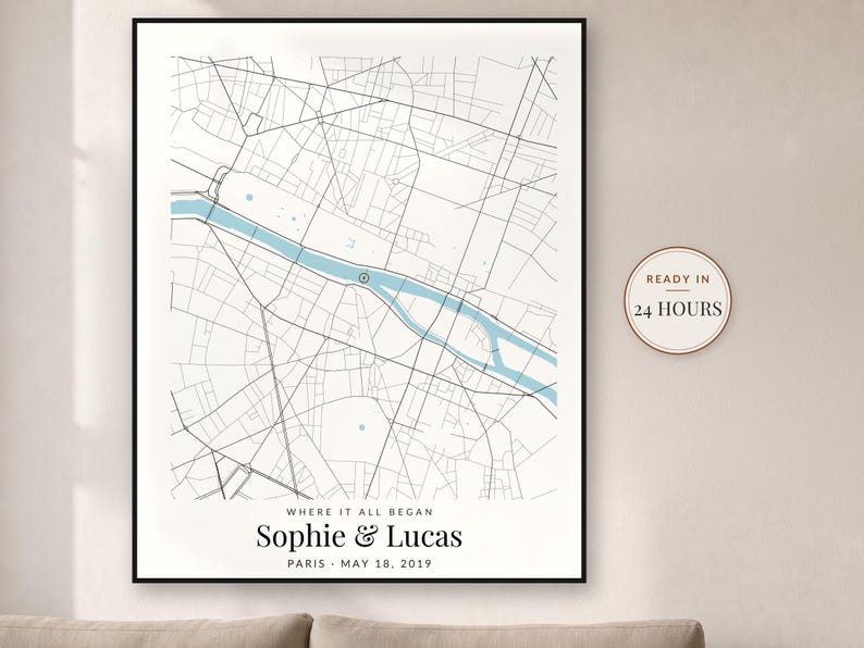 May include: A framed map print of Paris featuring black street lines and a light blue river. The text reads WHERE IT ALL BEGAN, Sophie & Lucas, PARIS, MAY 18, 2019. A circular badge on the right side displays the text READY IN 24 HOURS.