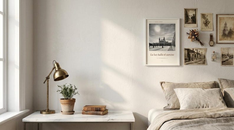 Op de afbeelding: Een ingelijste zwart-witprint met een gebouw en de tekst La luz halla el camino, weergegeven aan een muur naast verschillende kleinere vintage prints, een gedroogd boeket bloemen, een polshorloge en een klein glazen flesje.