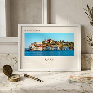 May include: A white framed print featuring a landscape photograph of the Greek island Kastellorizo with colorful buildings by the blue sea. The text reads Kastellorizo, Yunanistan, siga siga, slowly, slowly, and photography by Janet Stiber.