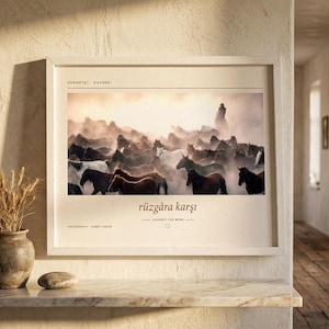 Op de afbeelding: Een ingelijste horizontale wandkunstprint met een foto van een kudde paarden die door stof rent. De tekst luidt HERMET&Ccedil;İ | KAYSERİ, r&uuml;zg&acirc;ra karşı, AGAINST THE WIND en PHOTOGRAPHY AHMET ZİREK. De lijst is gemaakt van lichtgekleurd hout.