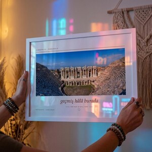 Puede incluir: Una fotograf&iacute;a de paisaje enmarcada en blanco que muestra el teatro antiguo de Hier&aacute;polis en Pamukkale. La impresi&oacute;n incluye el texto Hierapolis Pamukkale en la parte superior y la frase ge&ccedil;miş h&acirc;l&acirc; burada con la traducci&oacute;n The past is still here.