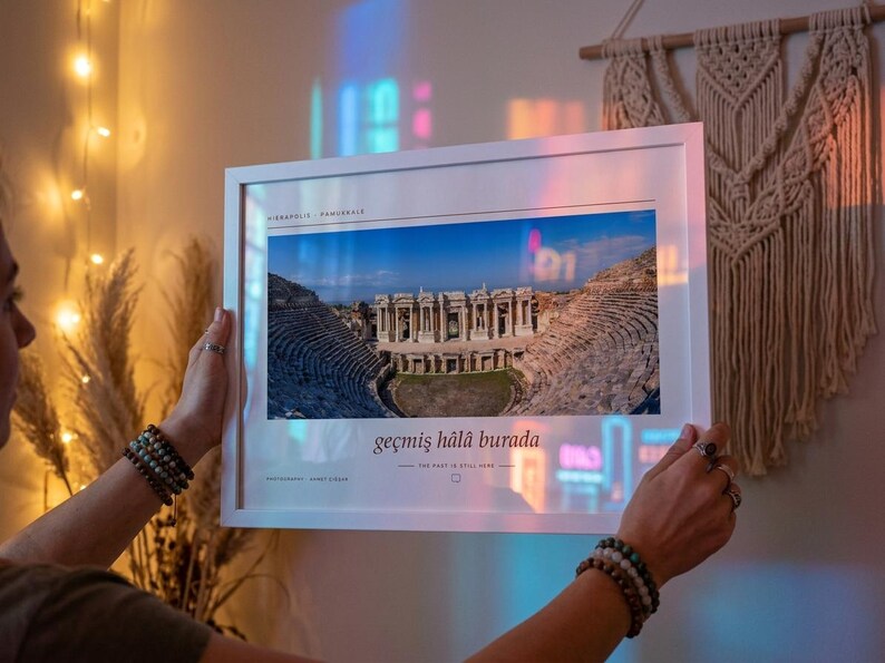 Puede incluir: Una fotograf&iacute;a de paisaje enmarcada en blanco que muestra el teatro antiguo de Hier&aacute;polis en Pamukkale. La impresi&oacute;n incluye el texto Hierapolis Pamukkale en la parte superior y la frase ge&ccedil;miş h&acirc;l&acirc; burada con la traducci&oacute;n The past is still here.