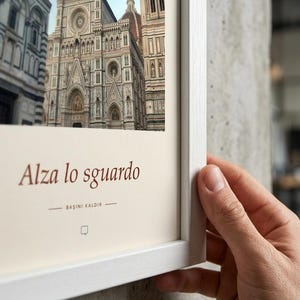 Puede incluir: Una l&aacute;mina de arte enmarcada con una fotograf&iacute;a de la fachada de la catedral de Florencia en Italia. La impresi&oacute;n incluye el texto Alza lo sguardo y BAŞINI KALDIR en letras de color marr&oacute;n oscuro sobre un fondo crema, en un marco de madera blanca.