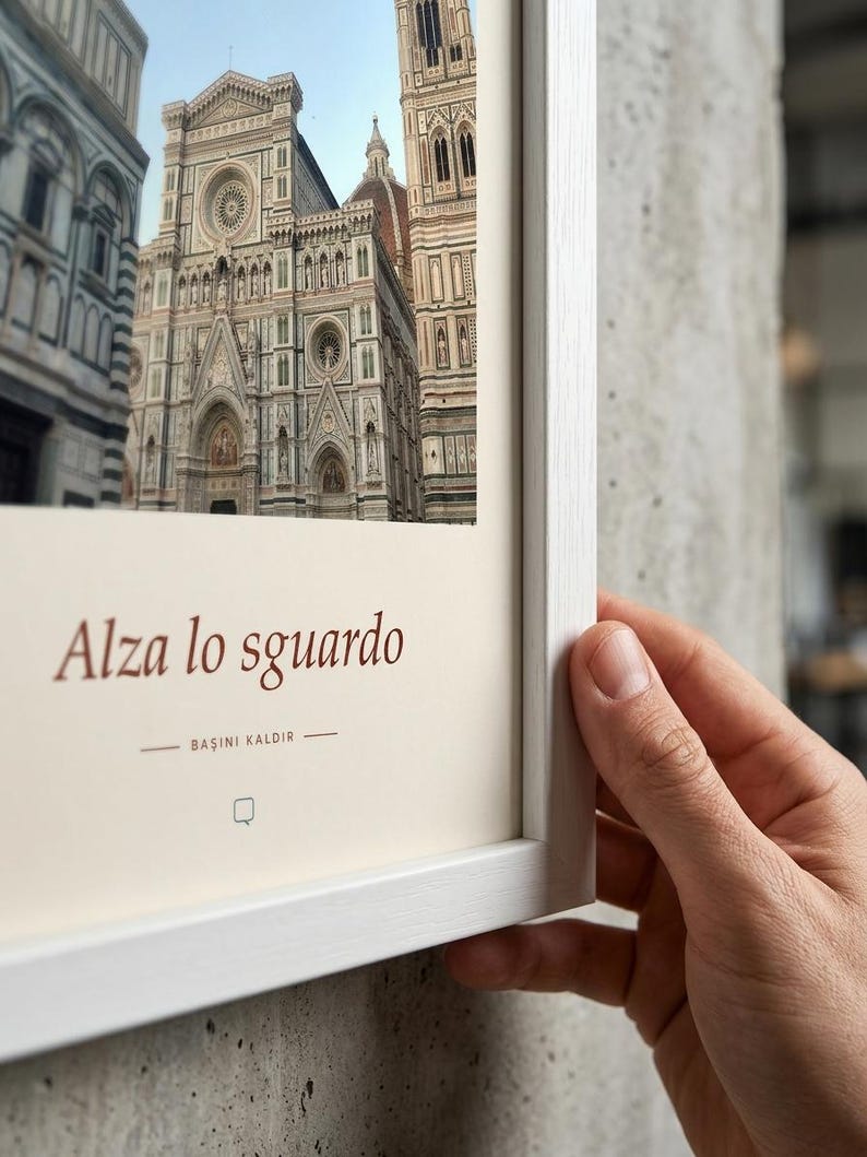 Puede incluir: Una l&aacute;mina de arte enmarcada con una fotograf&iacute;a de la fachada de la catedral de Florencia en Italia. La impresi&oacute;n incluye el texto Alza lo sguardo y BAŞINI KALDIR en letras de color marr&oacute;n oscuro sobre un fondo crema, en un marco de madera blanca.
