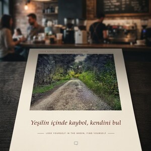 Puede incluir: Una impresi&oacute;n rectangular que presenta una fotograf&iacute;a de un camino de grava que serpentea a trav&eacute;s de un bosque denso. Debajo de la imagen, el texto dice: "Yeşilin i&ccedil;inde kaybol, kendini bul" y "LOSE YOURSELF IN THE GREEN, FIND YOURSELF" con un icono de burbuja.