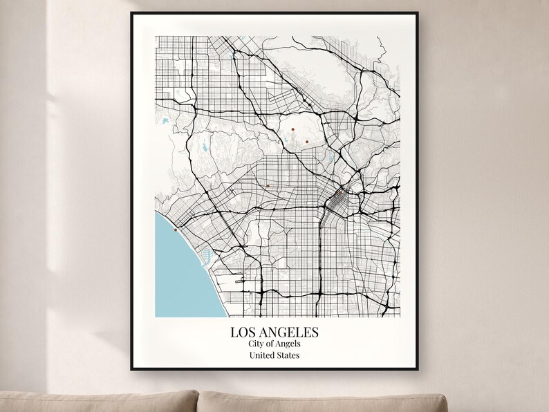 May include: A framed wall art print featuring a black and white street map of Los Angeles, California. The map displays a grid of roads, a light blue coastline, and the text LOS ANGELES, City of Angels, United States at the bottom.