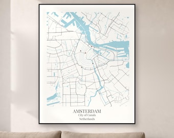 May include: A framed map print of Amsterdam, Netherlands, featuring black street lines and light blue water canals on a white background. The text at the bottom reads AMSTERDAM, City of Canals, Netherlands, with small red dots marking specific locations.
