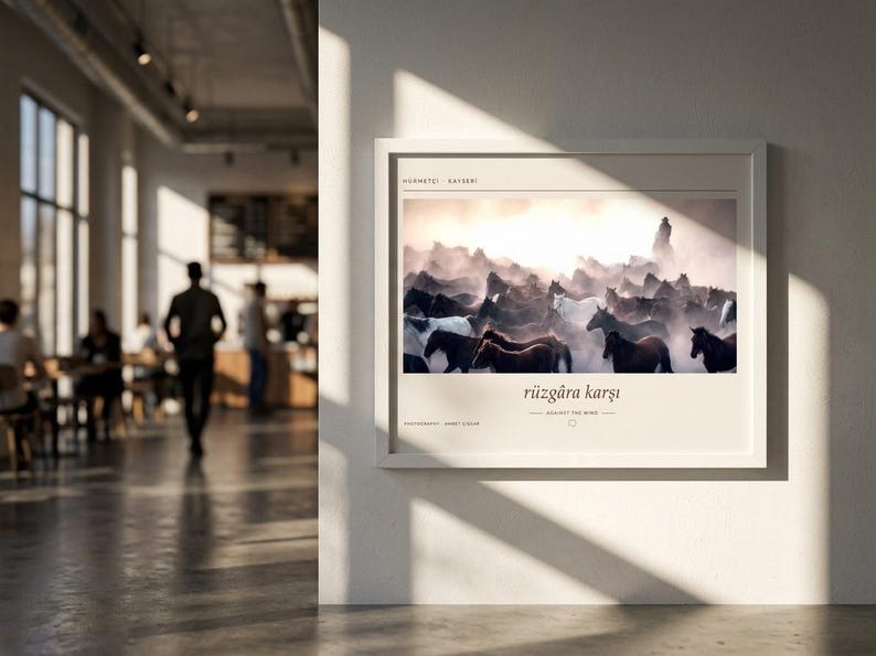 Op de afbeelding: Een ingelijste horizontale wandkunstprint met een foto van een kudde paarden die bij zonsondergang door stof rent. De tekst "H&uuml;rmet&ccedil;i - Kayseri" staat bovenaan en "r&uuml;zg&acirc;ra karşı" met "AGAINST THE WIND" staat onder de afbeelding gedrukt.