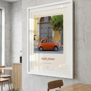 May include: A framed wall art print featuring a photograph of a small orange vintage car parked in front of a yellow building with a dark wooden door. The print includes the text SICILIA ITALIA at the top and vado piano at the bottom.