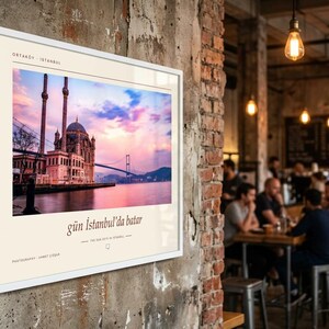 May include: A framed wall print featuring a photograph of the Ortak&ouml;y Mosque in Istanbul at sunset, with the text "ORTAK&Ouml;Y - ISTANBUL", "g&uuml;n İstanbul'da batar", and "THE SUN SETS IN ISTANBUL" printed in black on a cream-coloured border.