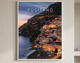May include: A vertical wall art print featuring a twilight landscape of Positano, Italy. The image displays a cliffside town with illuminated buildings, a dark mountain backdrop, and a calm sea. Text reads: COSTIERA AMALFITANA, POSITANO, il blu della sera.