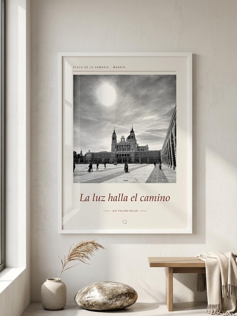 Op de afbeelding: Een ingelijste kunstdruk met een zwart-witfoto van de Plaza de la Armeria in Madrid. De tekst bovenaan luidt Plaza de la Armeria Madrid en onder de afbeelding staat La luz halla el camino met een kleinere regel tekst eronder.