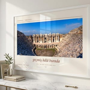 Puede incluir: Una impresi&oacute;n de arte mural horizontal enmarcada que presenta una fotograf&iacute;a del teatro antiguo de Hier&aacute;polis en Pamukkale. La impresi&oacute;n incluye el texto Hierapolis Pamukkale, la frase ge&ccedil;miş h&acirc;l&acirc; burada y la traducci&oacute;n The past is still here.