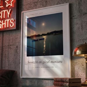 Puede incluir: Una l&aacute;mina enmarcada con un paisaje nocturno de un lago con un peque&ntilde;o bote y el reflejo de la luna. El texto dice SEYHAN BARAJ GOLU ADANA, Sessizlik en g&uuml;zel manzara y SILENCE IS THE MOST BEAUTIFUL VIEW en letras negras.