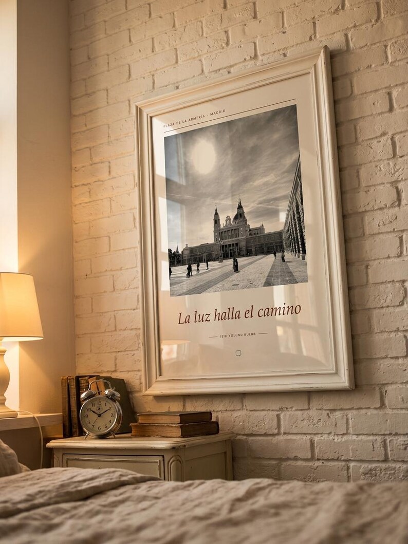 Op de afbeelding: Een ingelijste zwart-witfoto van de Plaza de la Armeria in Madrid, met een groot gebouw onder een felle zon. De print bevat de tekst Plaza de la Armeria Madrid, La luz halla el camino en 1018 yolunu bulur.