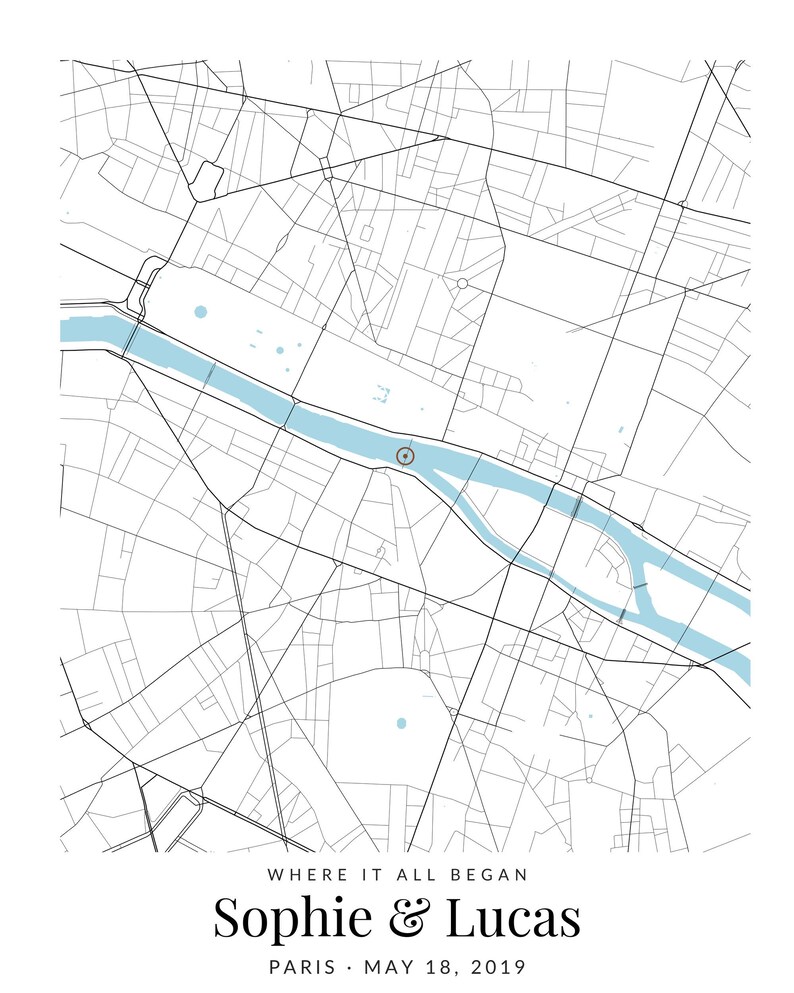 May include: A custom map print featuring a black and white street grid of Paris with a light blue river flowing through the center. A small circular marker highlights a specific location. Text reads: WHERE IT ALL BEGAN, Sophie & Lucas, PARIS, MAY 18, 2019.