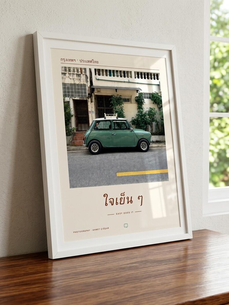 Pode incluir: Uma impress&atilde;o de arte emoldurada com uma fotografia de um carro compacto vintage verde-s&aacute;lvia estacionado numa rua em frente a um edif&iacute;cio. A impress&atilde;o inclui o texto tailand&ecirc;s "กรุงเทพฯ &middot; ประเทศไทย" no topo e "ใจเย็น ๆ" com a tradu&ccedil;&atilde;o inglesa "EASY DOES IT" abaixo.