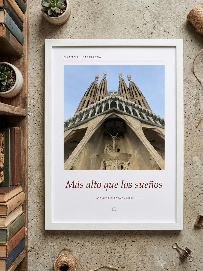 K&ouml;nnte beinhalten: Ein wei&szlig; gerahmter Kunstdruck mit einer Froschperspektive der Sagrada Familia in Barcelona. Der Text lautet oben EIXAMPLE BARCELONA und unter dem Bild M&aacute;s alto que los sue&ntilde;os sowie HAYALLERDEN DAHA Y&Uuml;KSEGE.