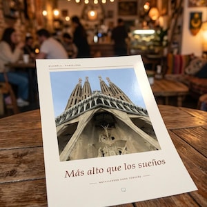 K&ouml;nnte beinhalten: Ein rechteckiger Druck mit einer Froschperspektive der Basilika Sagrada Familia in Barcelona. Der Text EIXAMPLE BARCELONA steht oben, w&auml;hrend der spanische Satz M&aacute;s alto que los sue&ntilde;os und ein t&uuml;rkischer Text darunter gedruckt sind.