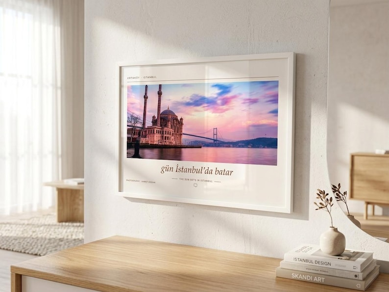 May include: A rectangular wall art print in a white frame featuring a photograph of the Ortak&ouml;y Mosque in Istanbul at sunset. The image displays a pink and blue sky over the Bosphorus bridge and water, with the text g&uuml;n İstanbul'da batar below.