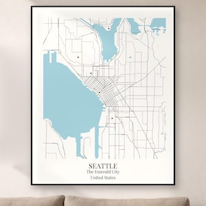 May include: A framed wall art print featuring a minimalist map of Seattle, Washington. The map displays light blue water bodies, black street lines, and small red markers. The text at the bottom reads SEATTLE, The Emerald City, United States.