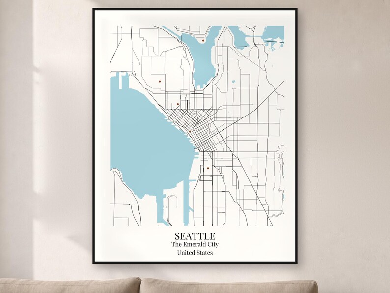 May include: A framed wall art print featuring a minimalist map of Seattle, Washington. The map displays light blue water bodies, black street lines, and small red markers. The text at the bottom reads SEATTLE, The Emerald City, United States.