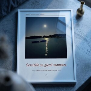 Puede incluir: Una l&aacute;mina de arte enmarcada en blanco con una fotograf&iacute;a de paisaje nocturno de un lago con dos barcas y una luna llena. El texto dice SEYHAN BARAJ GOLU ADANA, Sessizlik en guzel manzara y SILENCE IS THE MOST BEAUTIFUL VIEW con un icono.