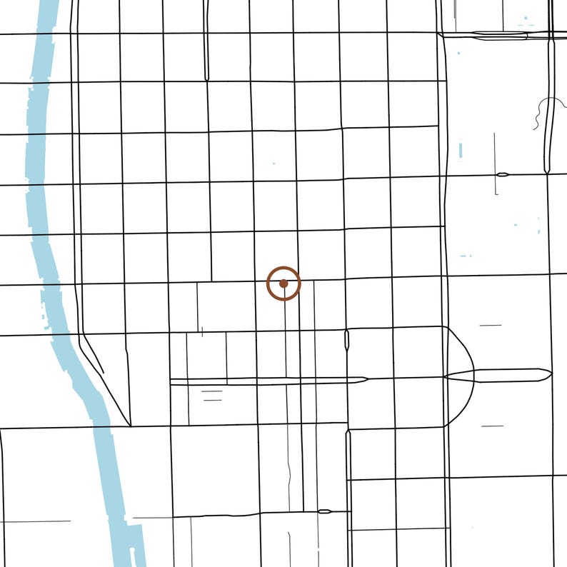 May include: A minimalist map illustration featuring a grid of thin black lines representing city streets, a light blue vertical band indicating a river on the left, and a single brown circular marker with a central dot in the middle.