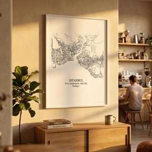 Puede incluir: Una l&aacute;mina de arte mural enmarcada que muestra un mapa de l&iacute;neas negras de Estambul, Turqu&iacute;a. El texto debajo del mapa dice: ISTANBUL, Two continents, one city, T&uuml;rkiye. La l&aacute;mina se exhibe en un marco blanco fino sobre una pared clara y un mueble de madera.