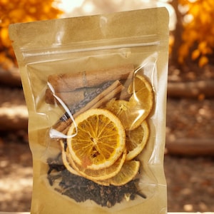 May include: A clear plastic pouch with a brown paper backing containing dried orange slices, whole cinnamon sticks, dark cloves, and sprigs of dried lavender. The pouch features a resealable zipper top and is filled with these aromatic botanical ingredients.