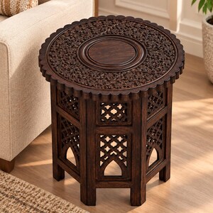 May include: A dark brown wooden side table with a circular top featuring intricate floral carvings and a scalloped edge. The base is hexagonal with open lattice panels and arched cutouts, providing a sturdy structure for this small furniture piece.